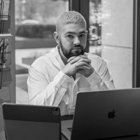 Artur Minvaleev seated at a café table with a laptop, looking at the camera